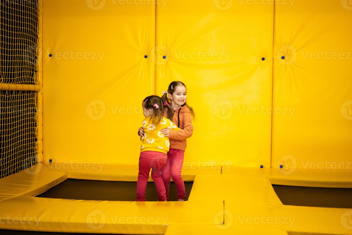 Siblings jumping on trampoline at yellow playground park. Sisters in motion during active entertaiments. photo