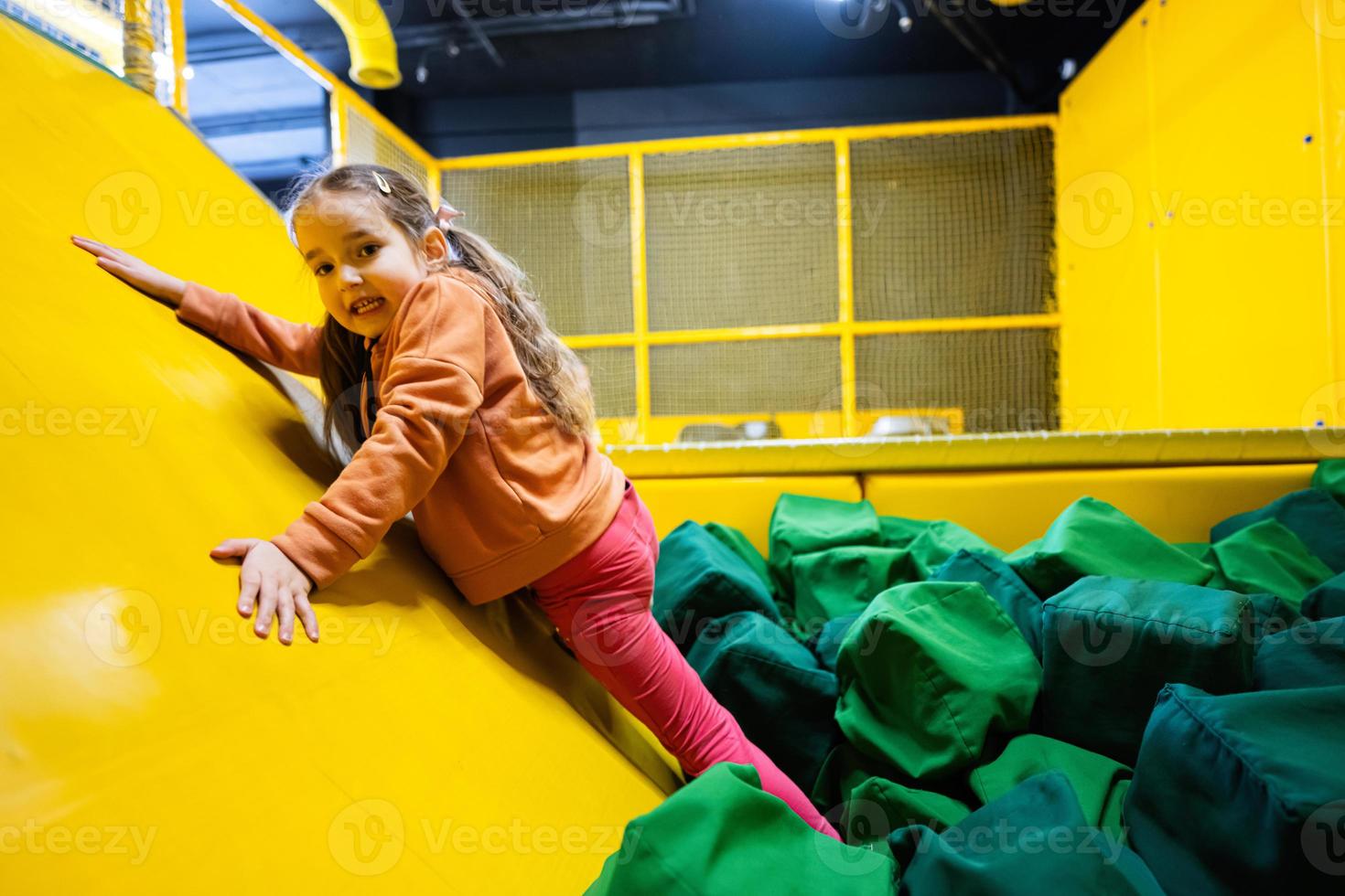 Little girl kid slide at yellow playground park. Child in active entertaiments. photo