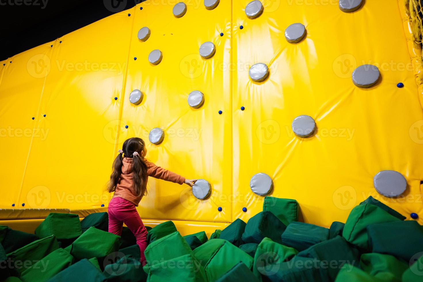 Little girl kid climbing wall at yellow playground park. Child in motion during active entertaiments. photo