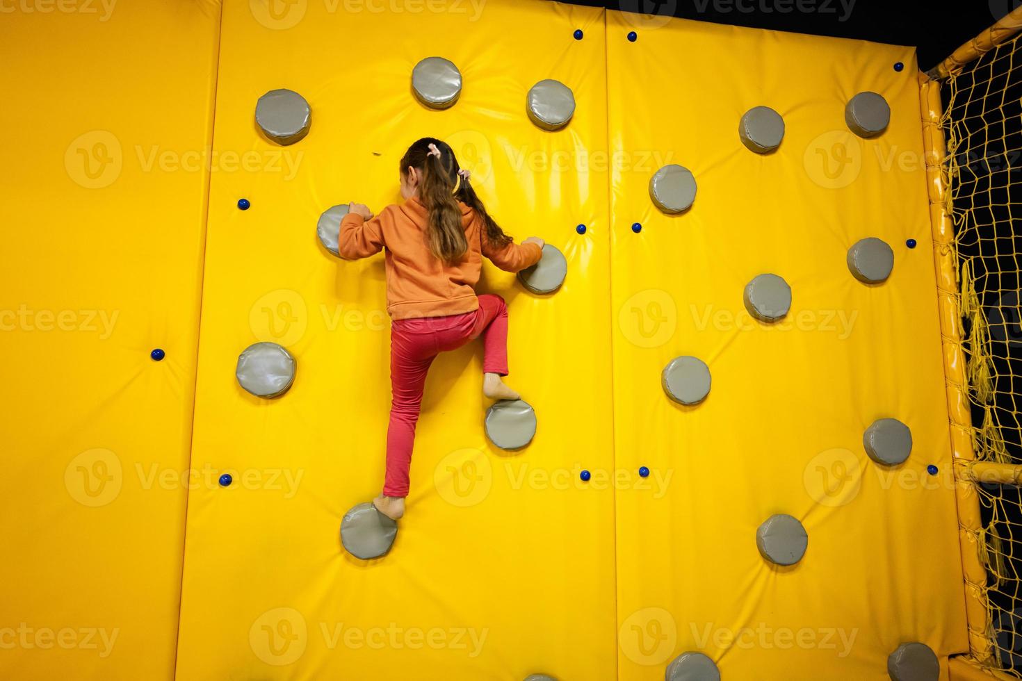 Little girl kid climbing wall at yellow playground park. Child in motion during active entertaiments. photo