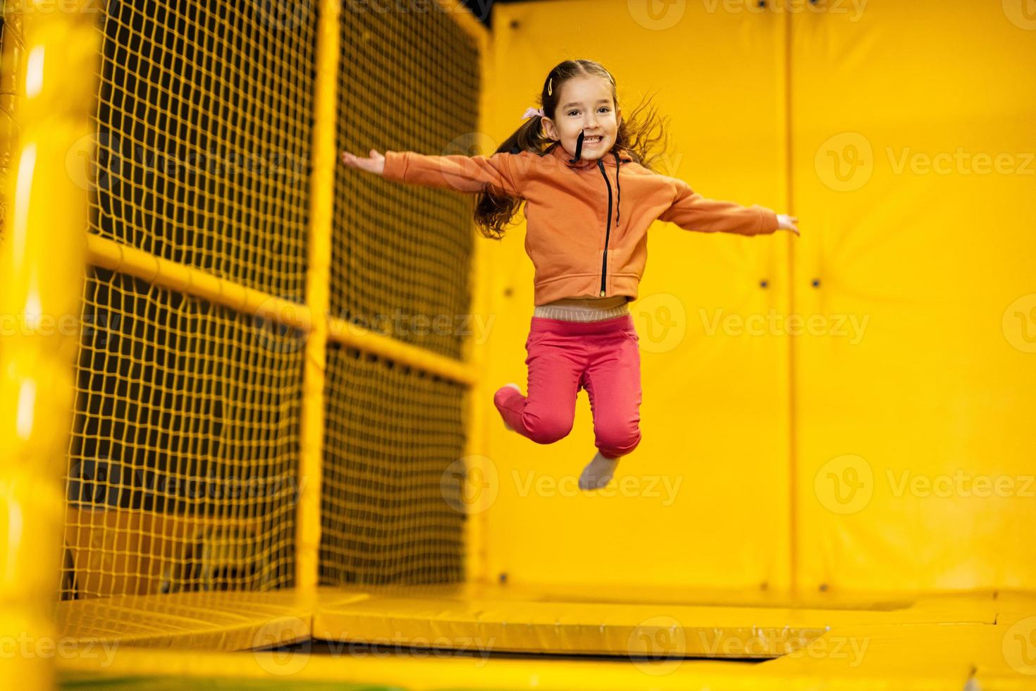 Little girl kid jumping on trampoline at yellow playground park. Child in motion during active entertaiments. photo
