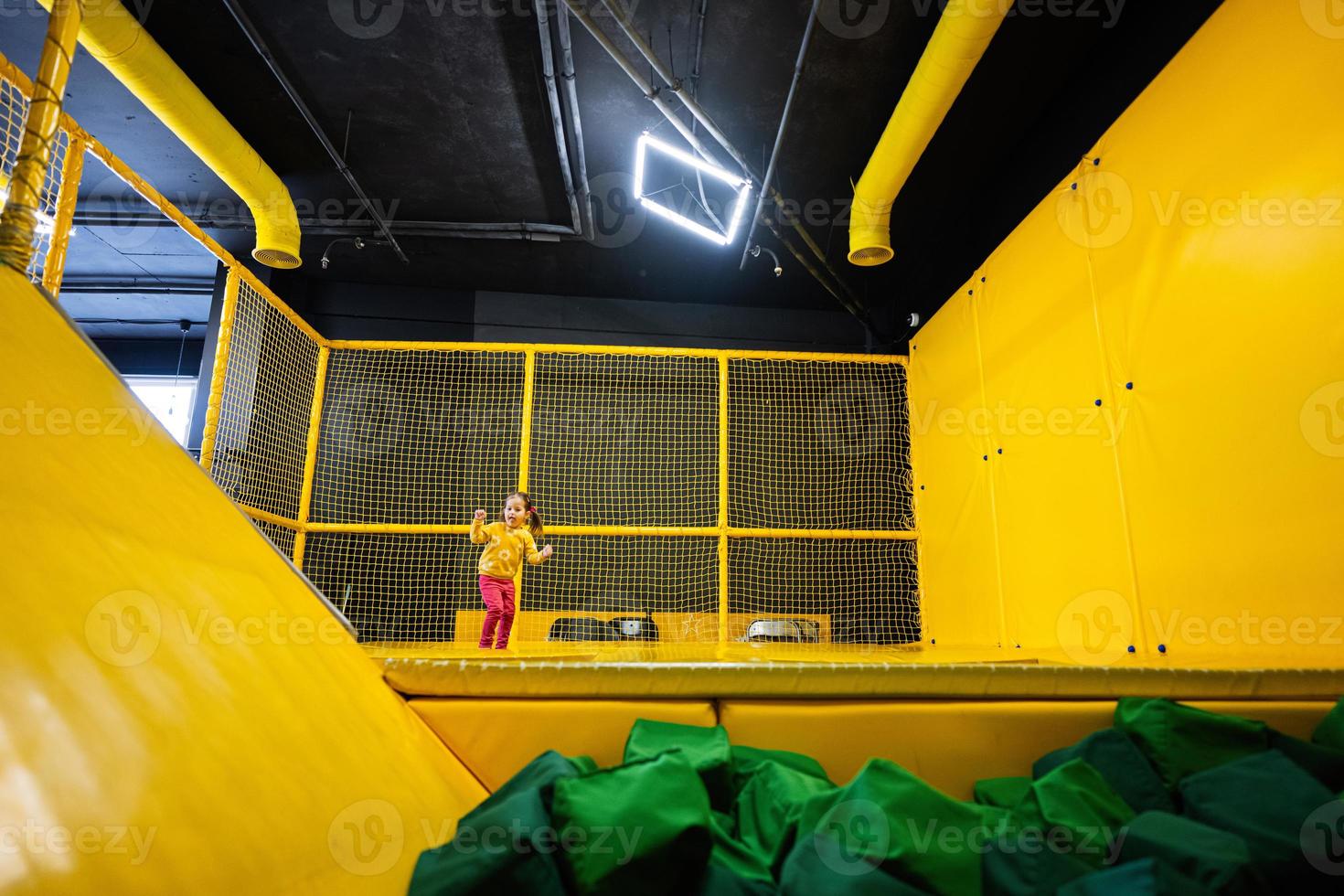 Little girl kid jumping on trampoline at yellow playground park. Child in motion during active entertaiments. photo