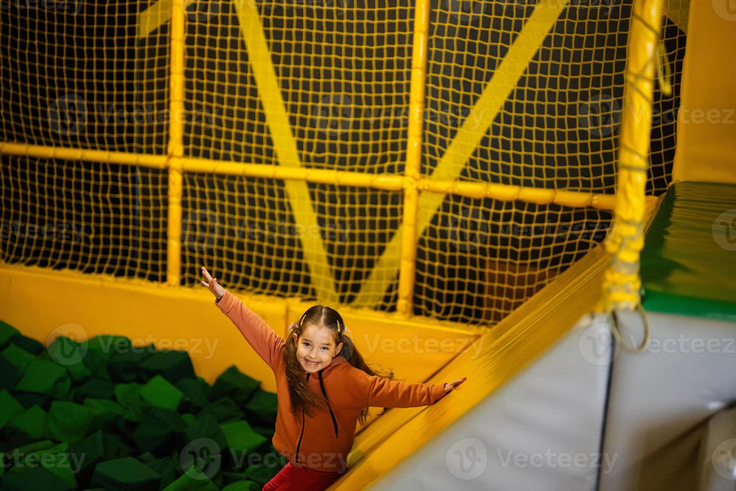 Little girl kid slide to green soft cubes at yellow playground park. Child in active entertaiments. photo