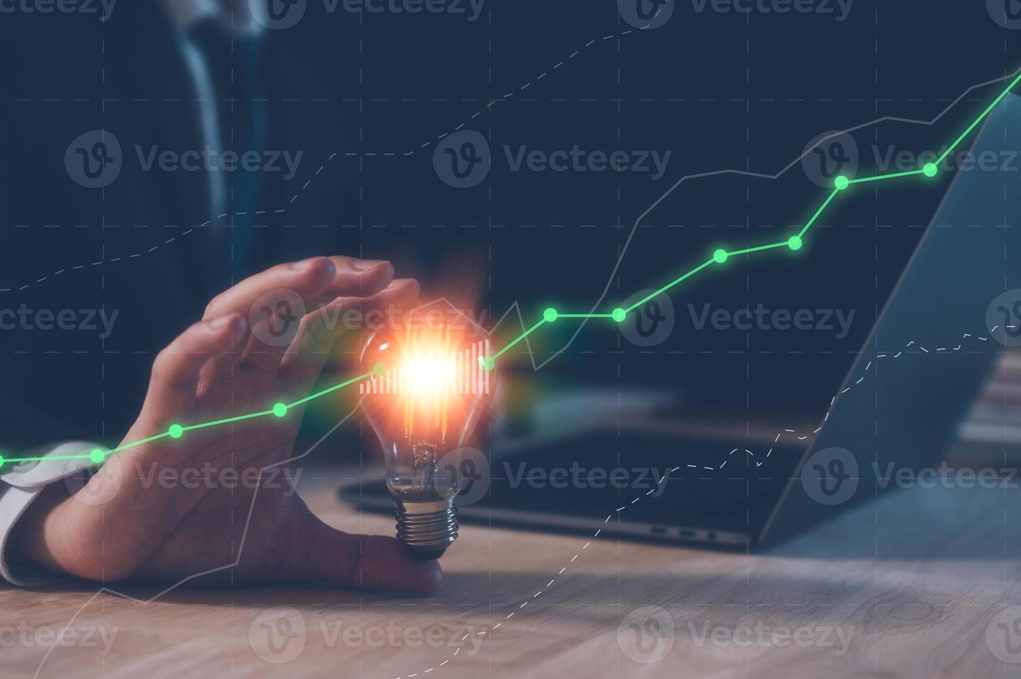 investment strategy and ideas concept, businessman holding light bulb with virtual trading  graph and working on computer laptop on table in office, saving and investment idea, creative new wealth. photo