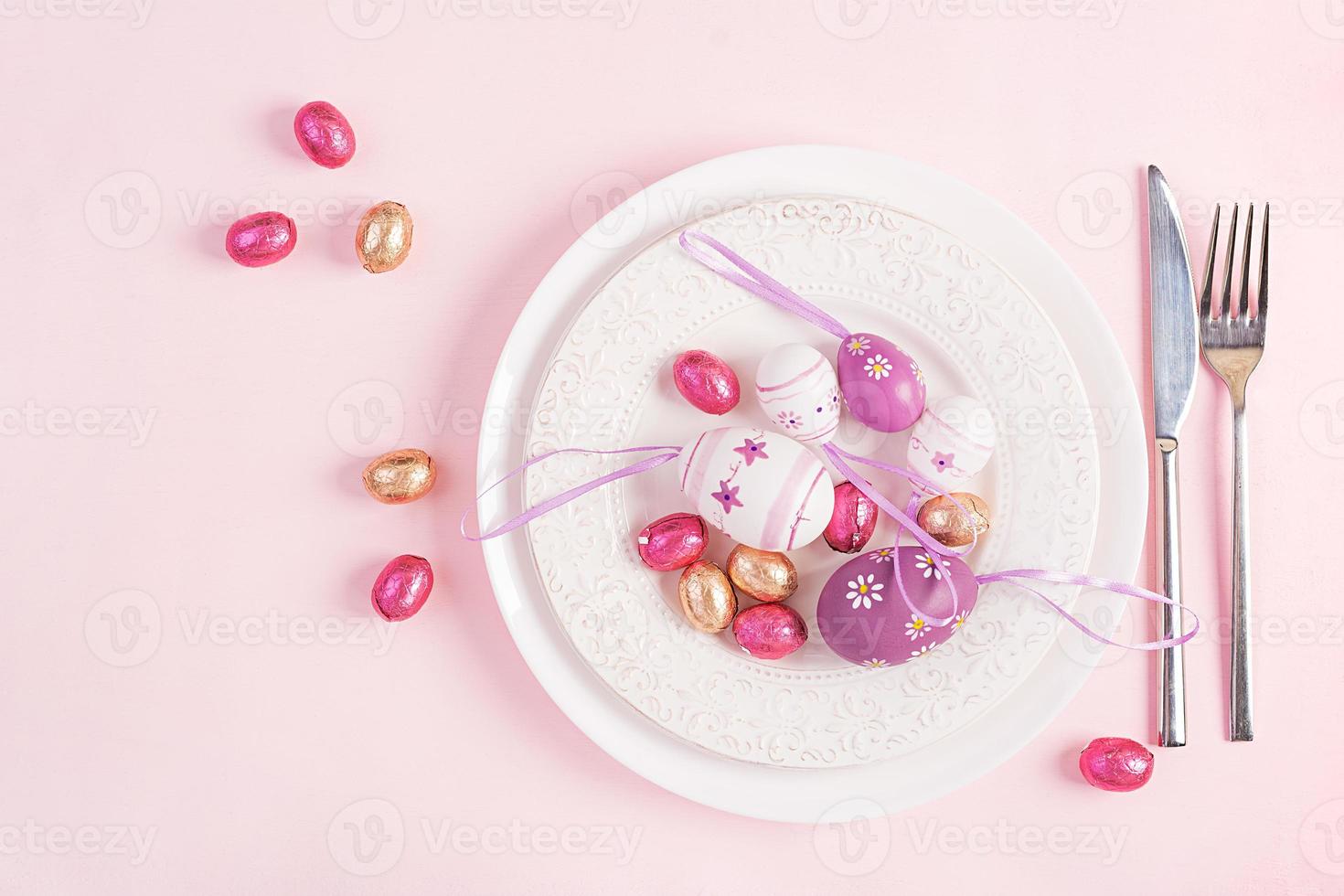 Happy Easter. Table setting for Easter holiday. Easter eggs, flower and cutlery on pink background. Top view, flat lay photo