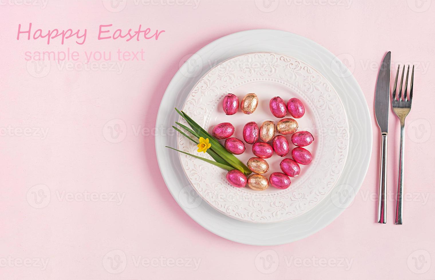Happy Easter. Table setting for Easter holiday. Easter eggs, flower and cutlery on pink background. Top view, flat lay photo