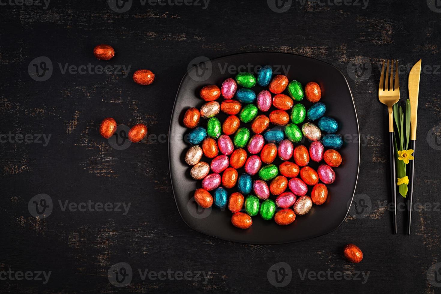 Happy Easter. Table setting for Easter holiday. Easter chocolate eggs and cutlery on dark background. Top view, flat lay photo