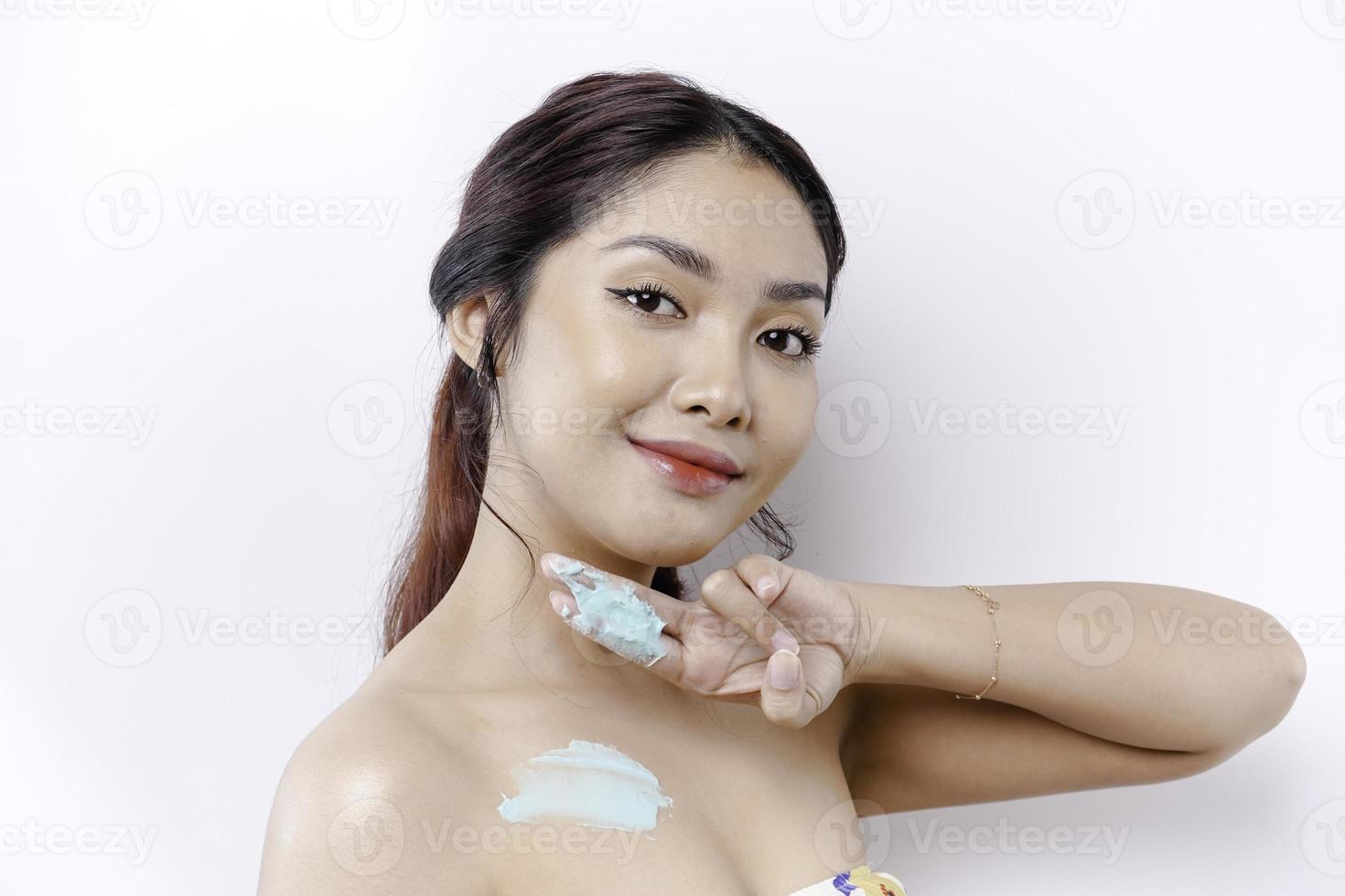 Skin Care Products Concept. Asian woman applying moisturizing lotion on body after shower, standing wrapped in towel, cropped image photo