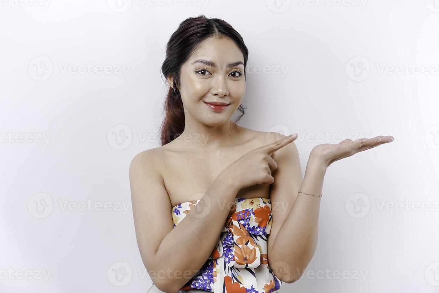 Excited Asian woman pointing at the copy space beside her, isolated by white background photo