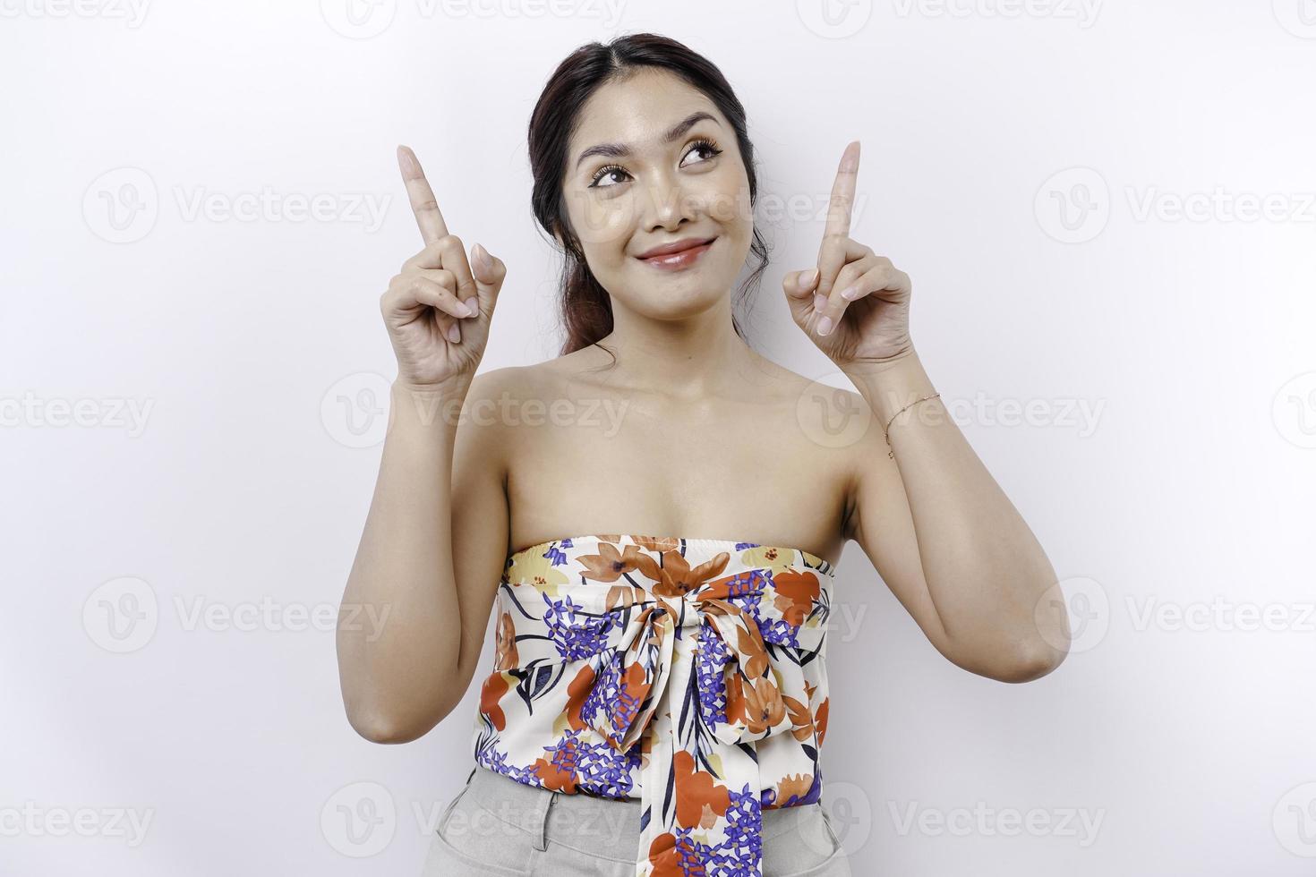 Excited Asian woman pointing at the copy space on top of her, isolated by white background photo