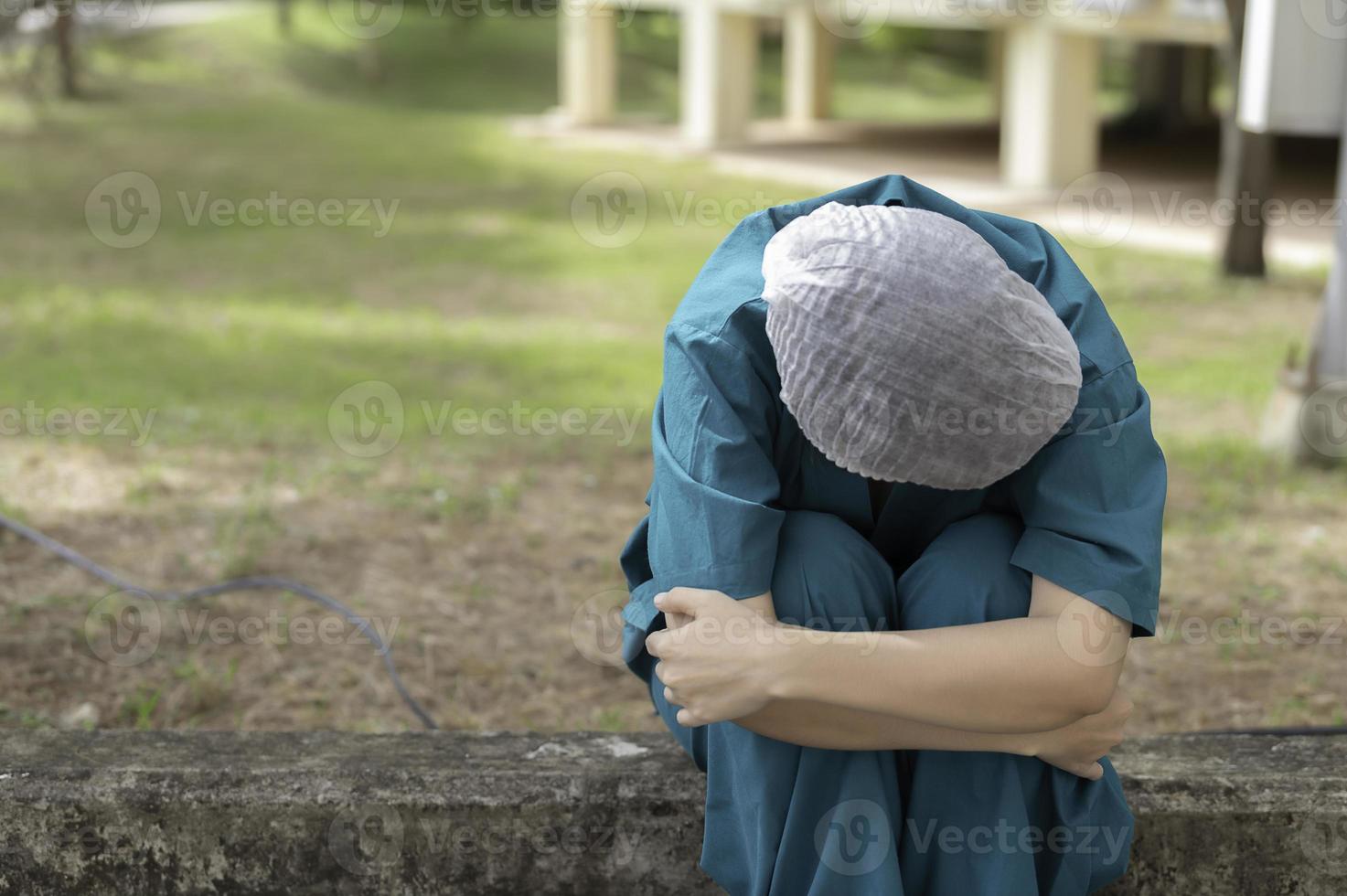 Tired depressed female asian scrub nurse wears face mask blue uniform sits on hospital floor,Young woman doctor stressed from hard work photo