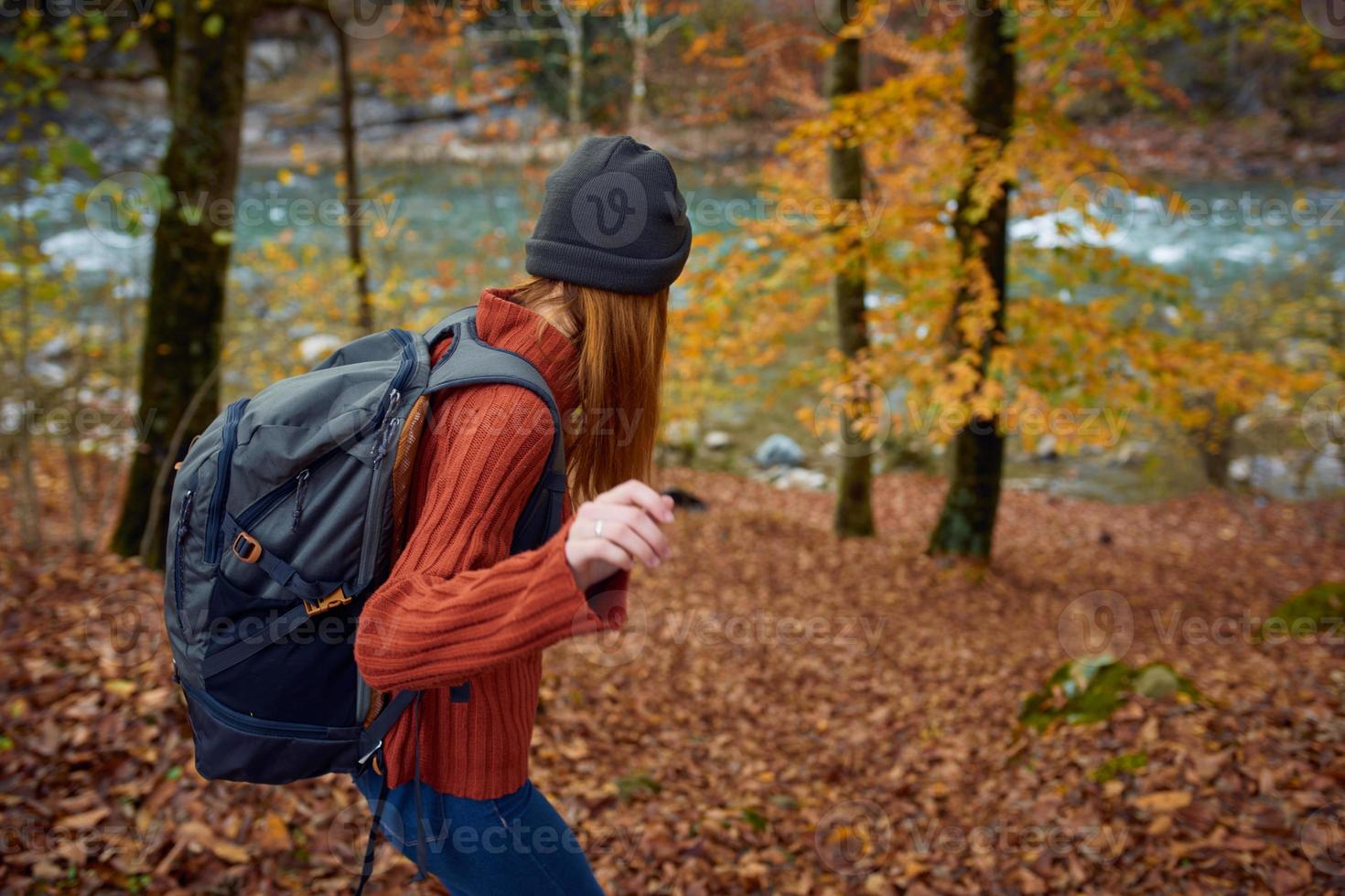 woman in a sweater with a backpack on her back near the river in the mountains and park trees autumn landscape photo