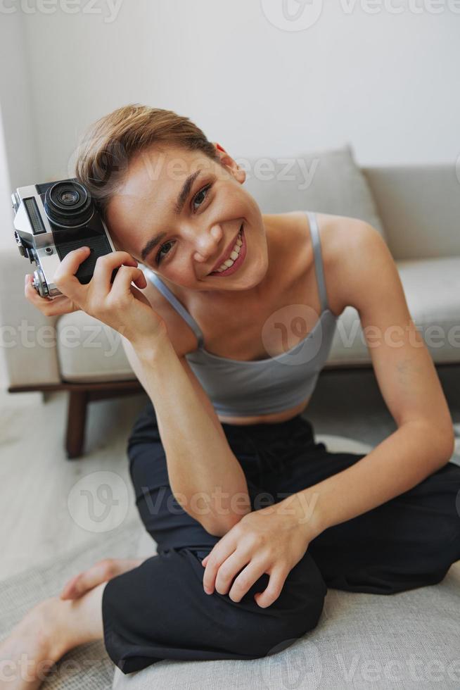 contento sonrisa mujer participación un antiguo cámara y tomando imágenes de sí misma como un fin de semana fotógrafo en hogar ropa con un corto Corte de pelo pelo sin filtros en un blanco fondo, gratis Copiar espacio foto