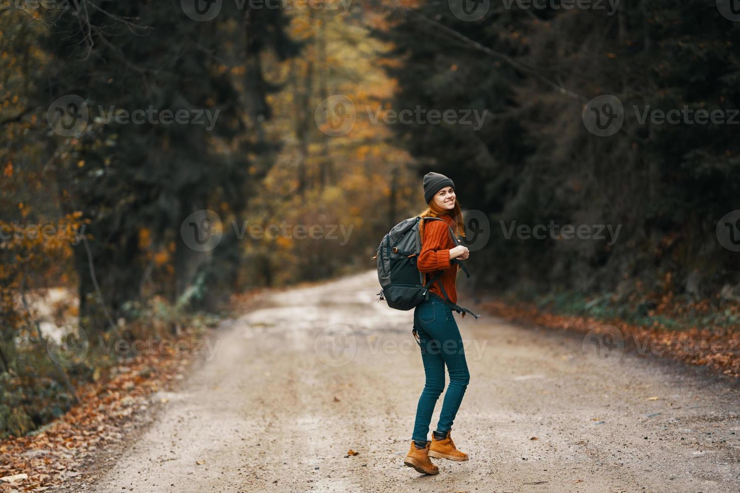 happy traveler with backpack walks on the road in autumn forest photo