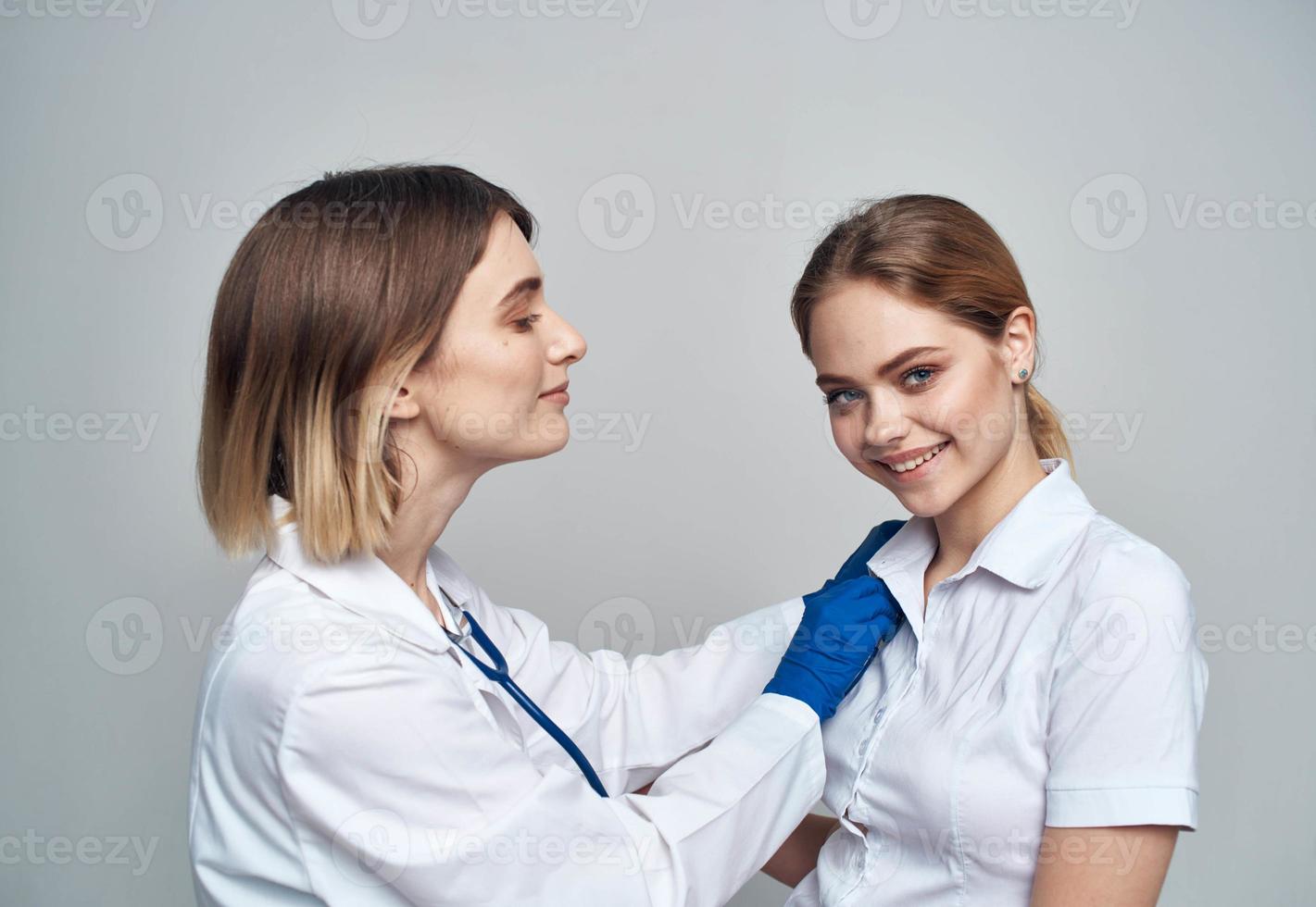 Happy woman doctor in blue gloves and female patient in white t-shirt stethoscope medical gown photo