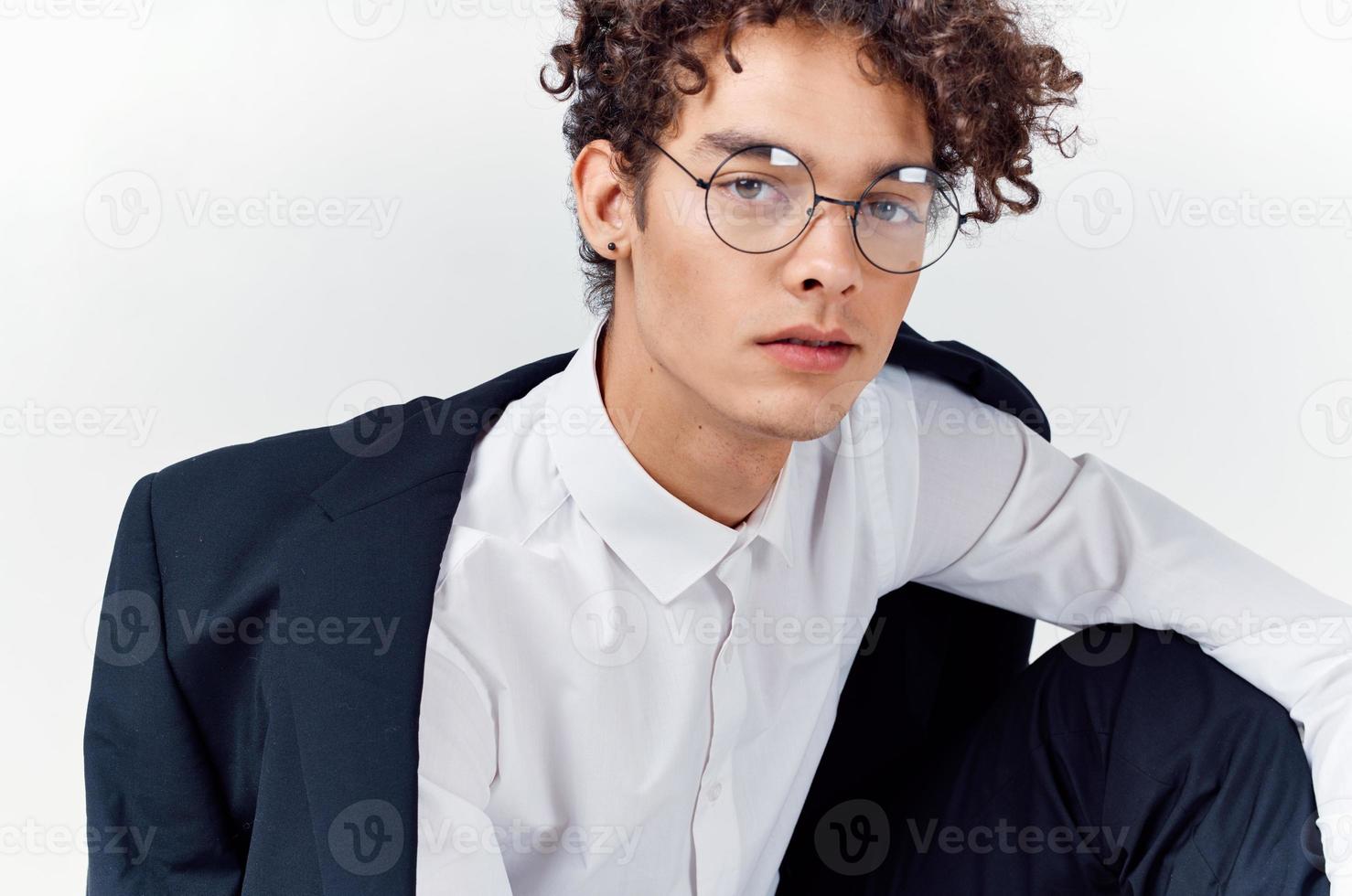 portrait of a curly-haired guy in a shirt in a jacket and glasses on a light background close-up photo