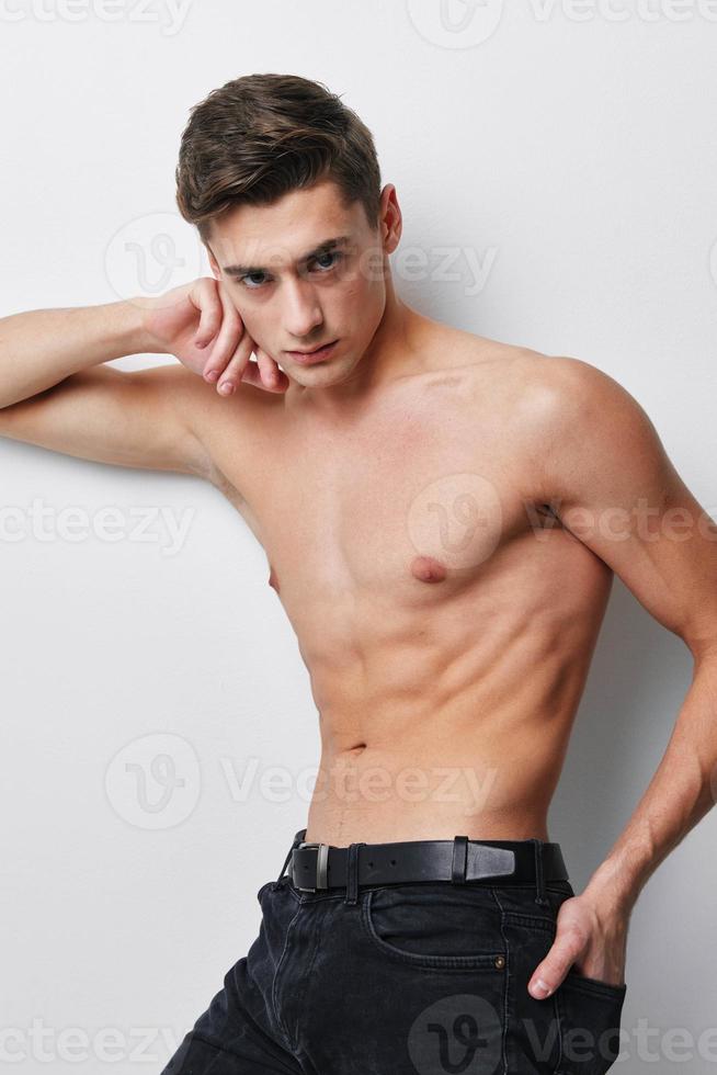 A sexy guy with a naked torso leaned to the side and holds his hand at his waist photo