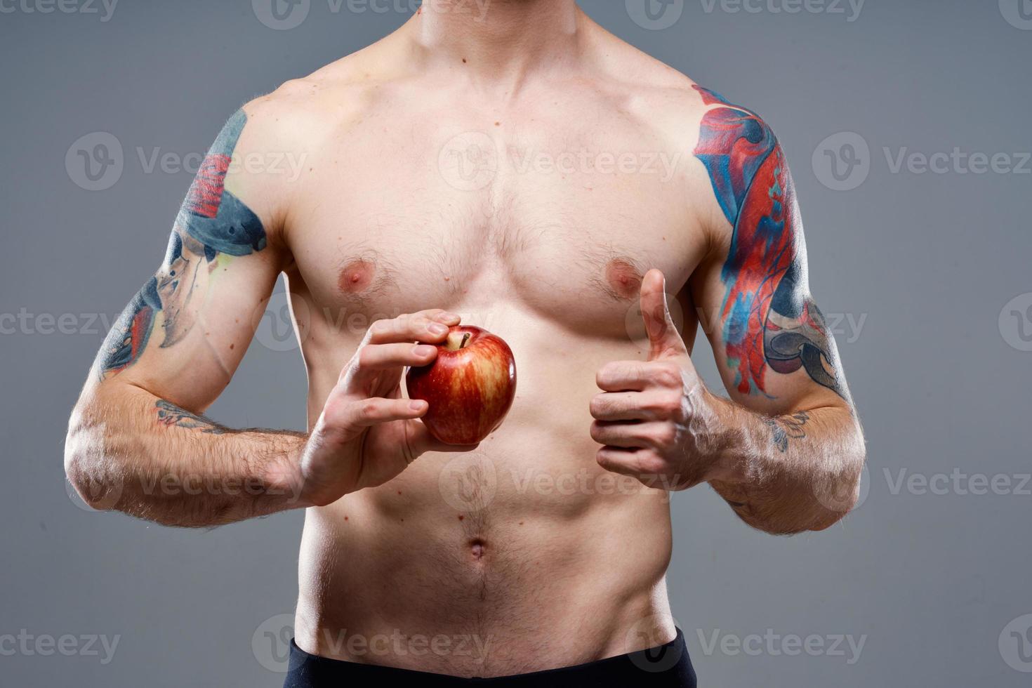 young man with apple and pumped up torso biceps man tattoo gray background cropped view photo