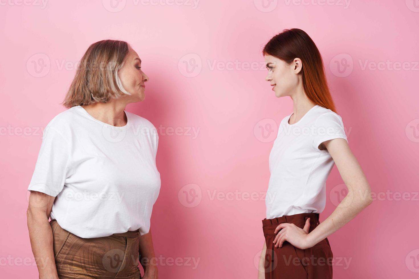 grandmother and granddaughter are standing side by side family friendship fun pink background photo