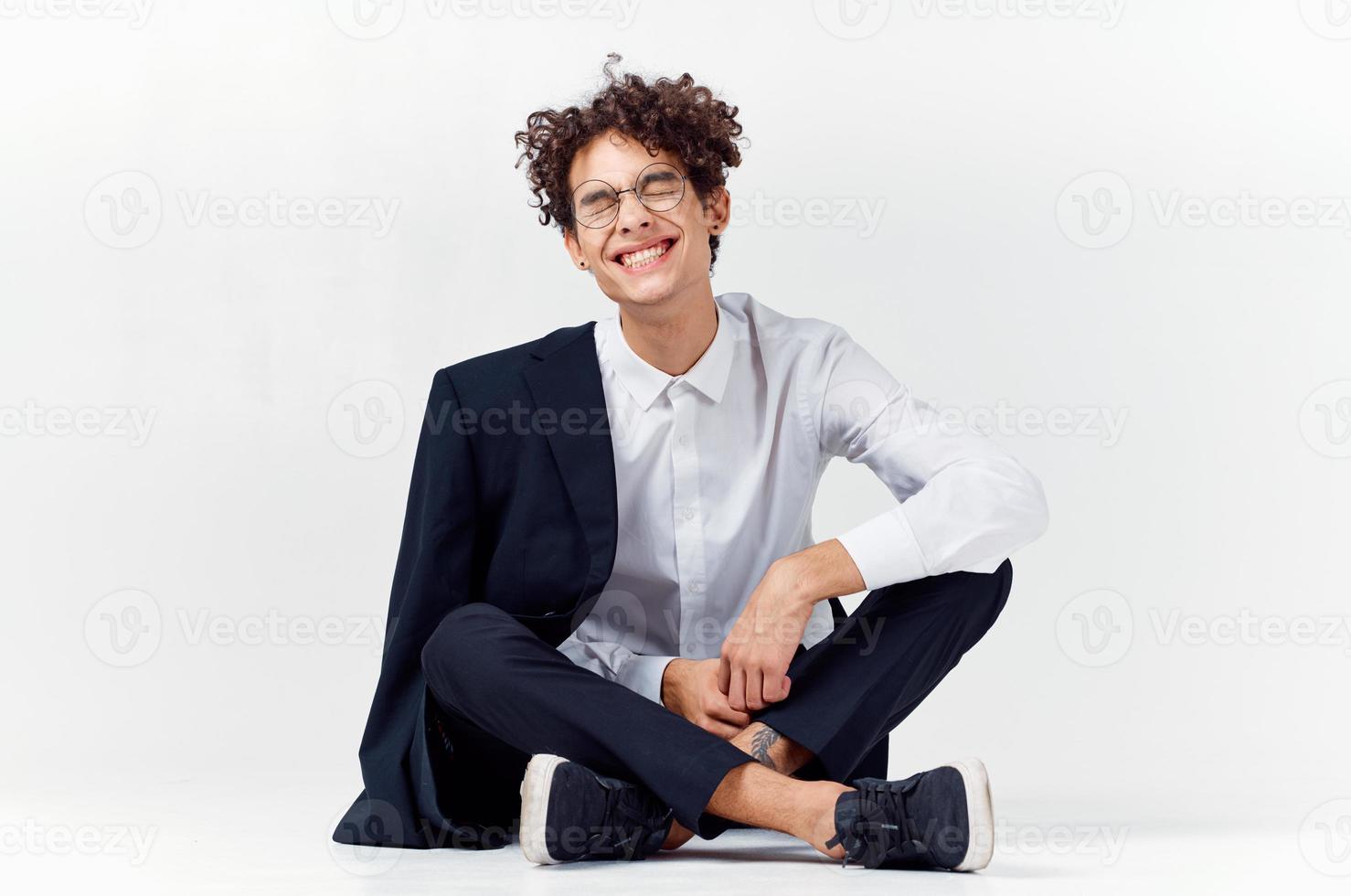 guy in a classic suit sits on the floor in a bright room glasses on the face photo