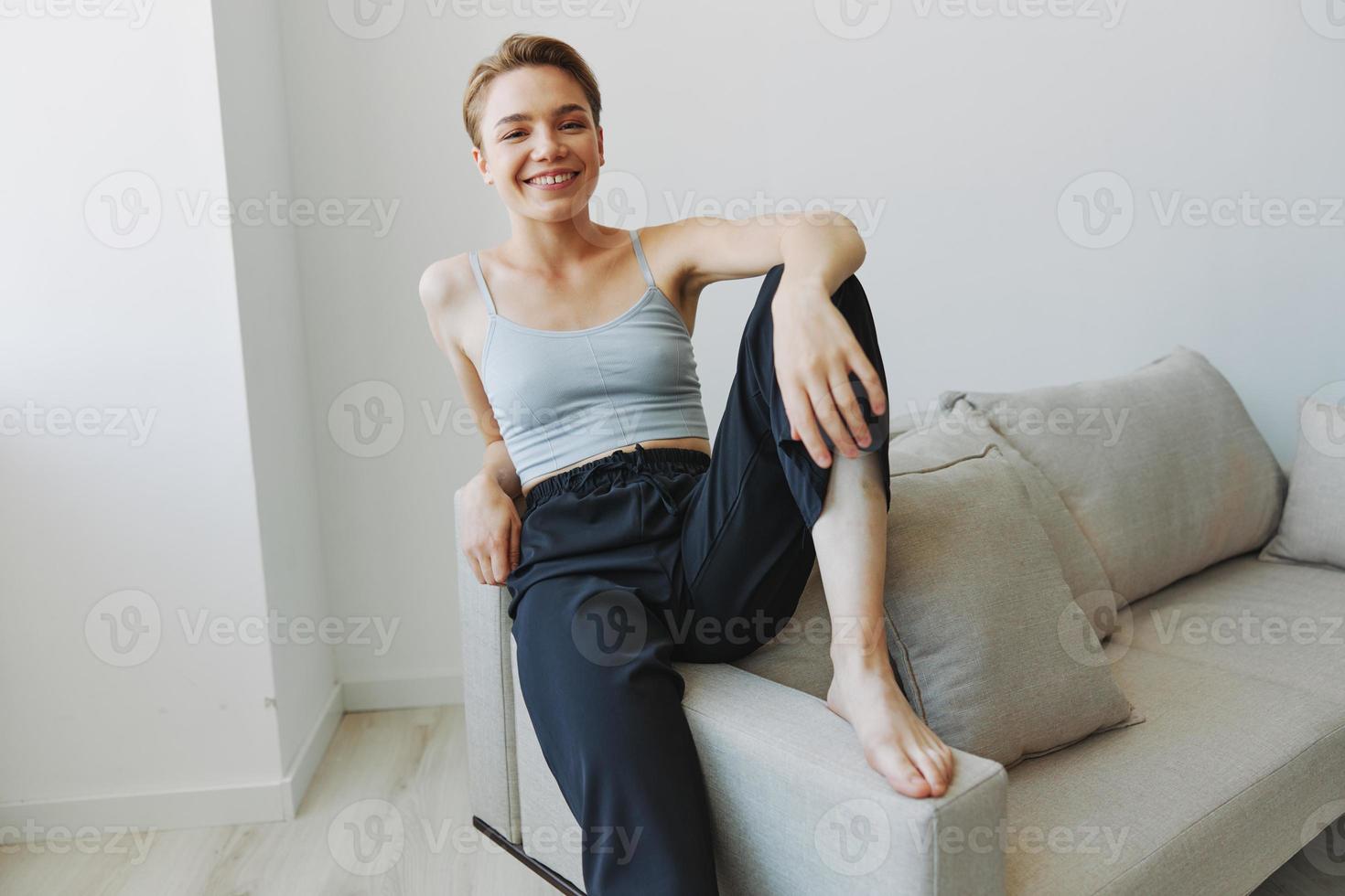 Teenage girl sitting on the couch at home smiling in home clothes and glasses with a short haircut, lifestyle without filters, free copy space photo