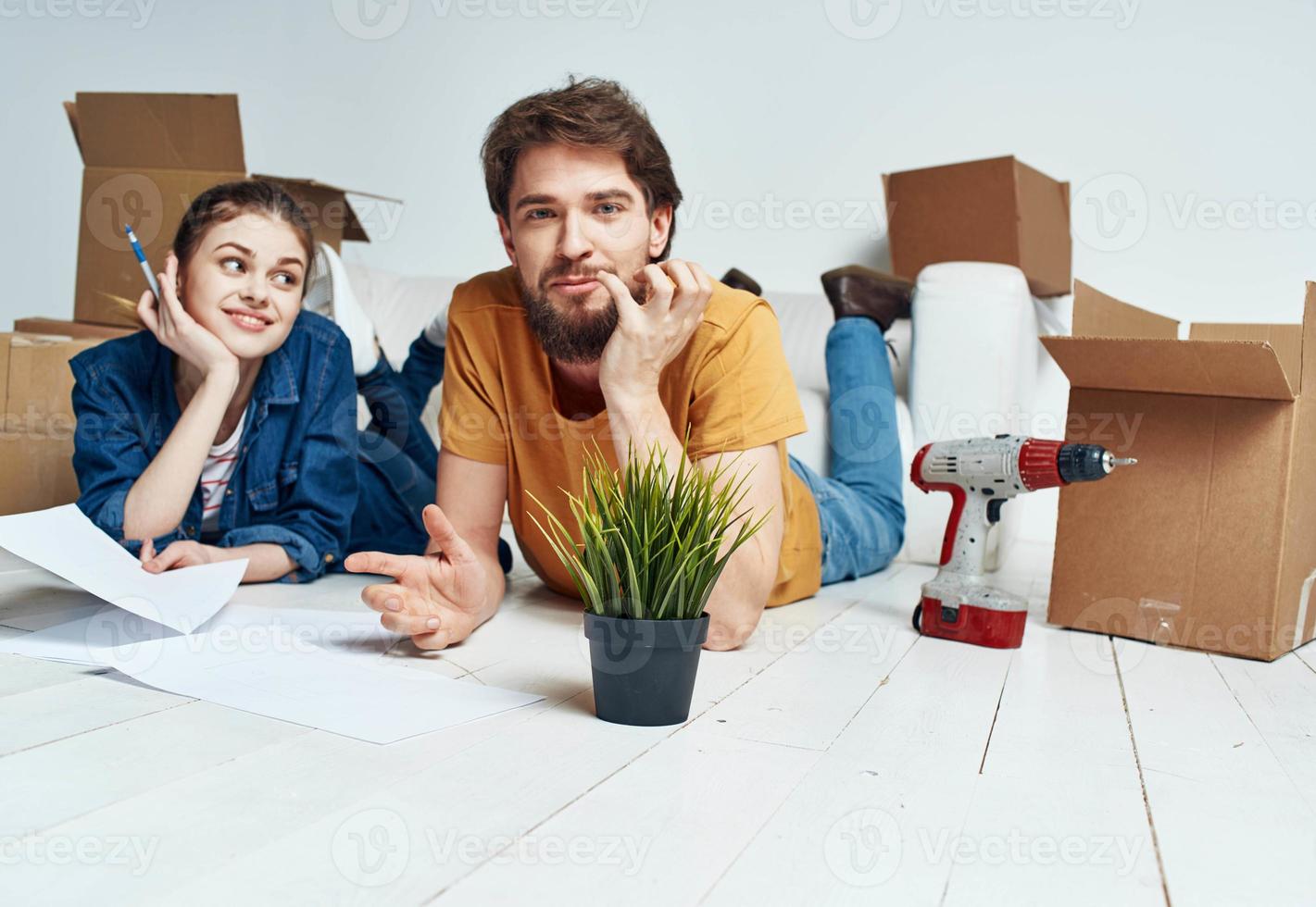 a man and a woman lie on the floor among boxes and a flower in a pot moving photo