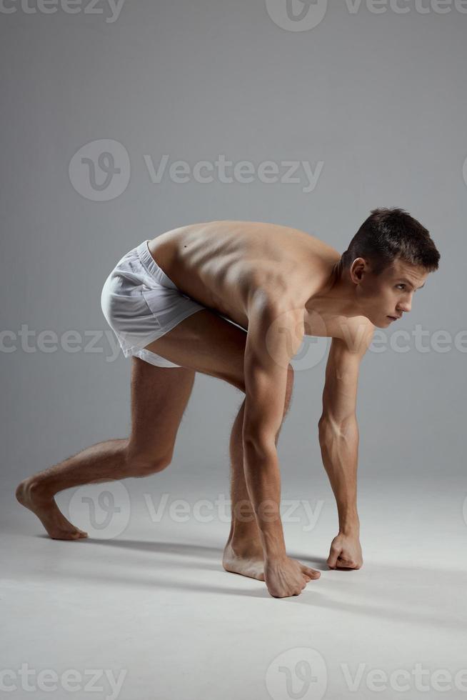 athlete with a pumped-up torso in white shorts on a gray background leaned forward photo