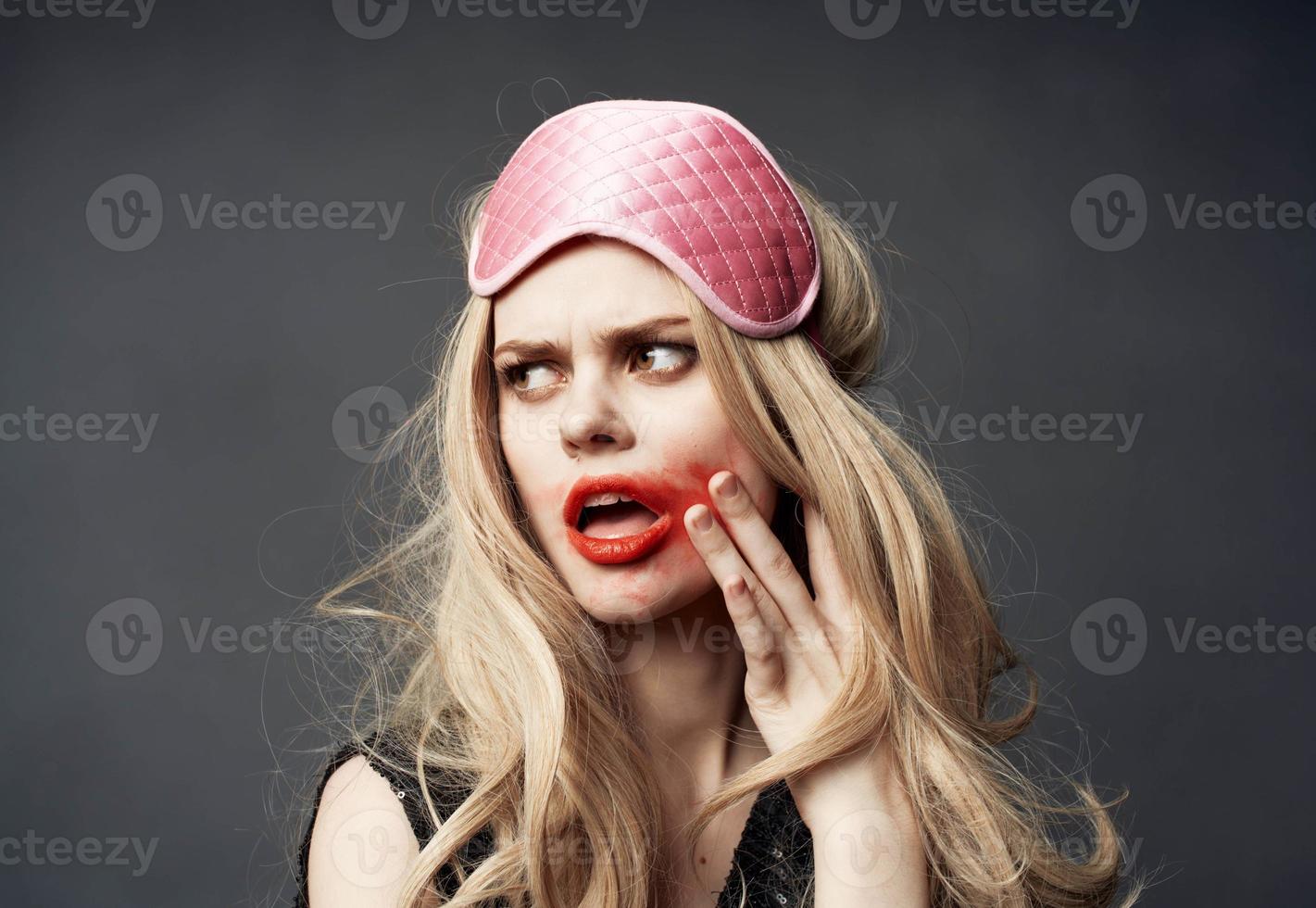 A blonde with bright makeup on her face and a pink sleep mask on her head photo