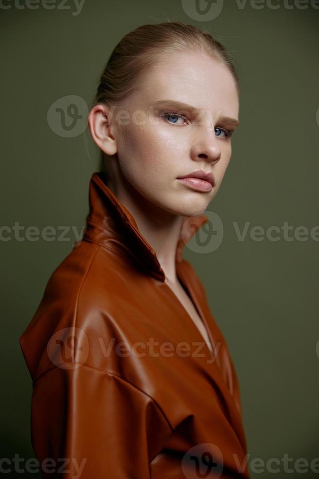 Elegant fashionable young blonde girl with blue eyes with evening makeup in a leather dress looks at the camera posing isolated for banner design. Studio portrait on a green background. Makeup concept photo