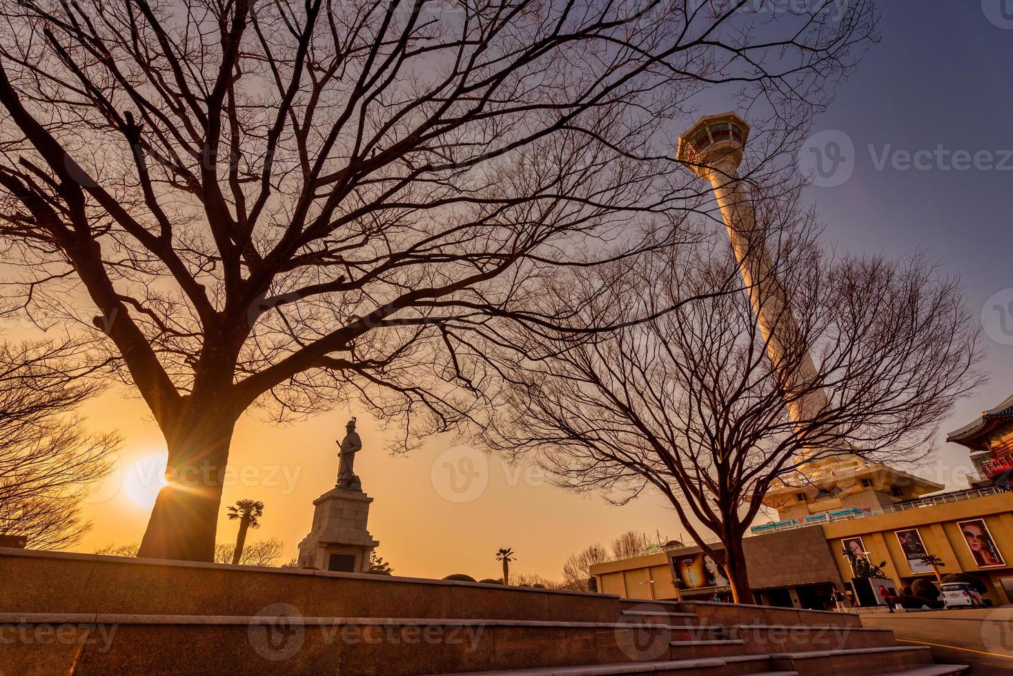 View of Busan tower with statue of Yi Sun-sin in front on blue sky background with trees. photo