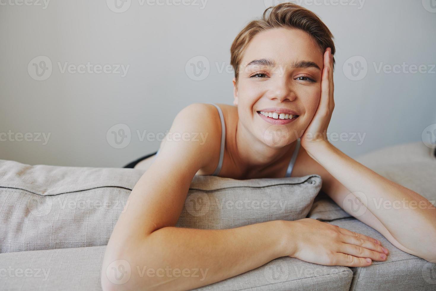 contento mujer sonrisa acostado a hogar en el sofá relajante en un fin de semana a hogar con un corto Corte de pelo pelo sin filtros en un blanco fondo, gratis Copiar espacio foto