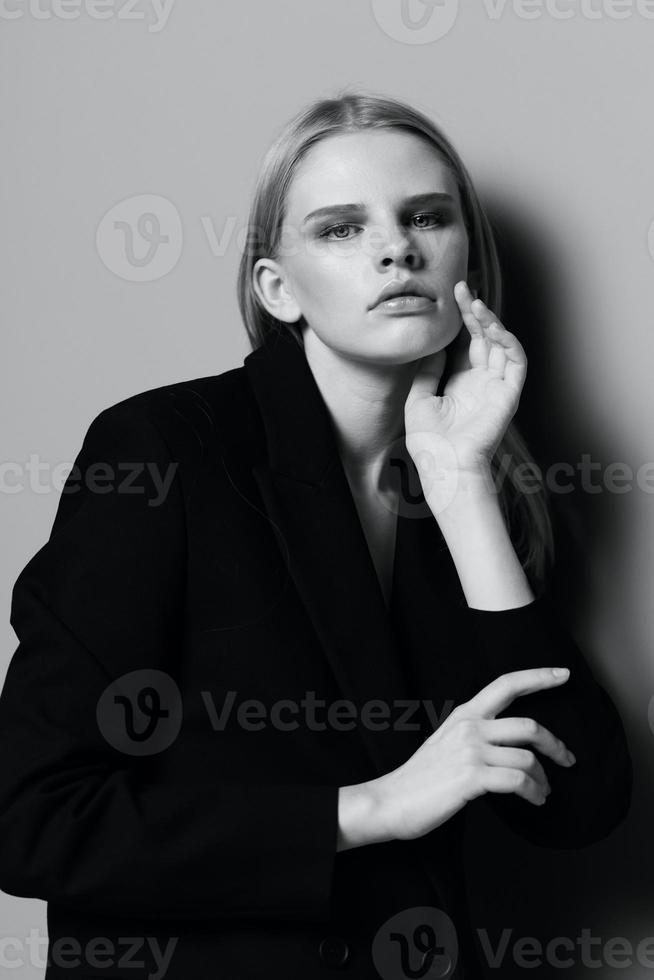 Elegant girl puts her hand to her face tucks her hair behind her ear poses in the studio in black and white style photo