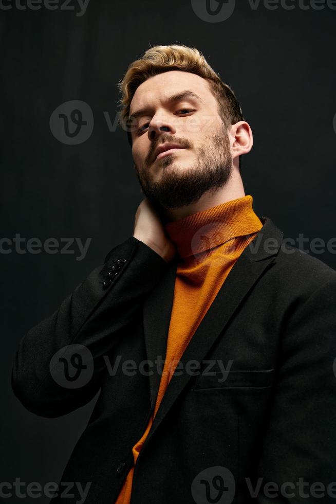 confident young blond man in jacket orange sweater on dark background raised his head up cropped view photo