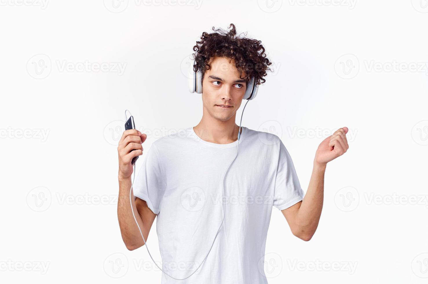 gracioso chico con Rizado pelo en un blanco camiseta escucha a música tecnología entretenimiento foto