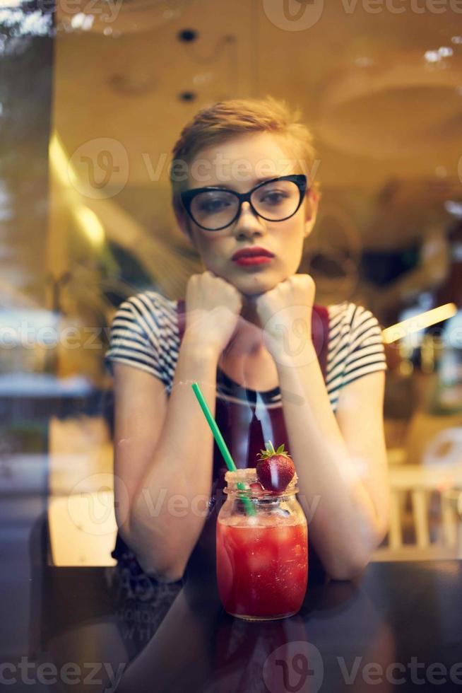 a woman with a short hairstyle sits in a cafe alone with a cocktail photo