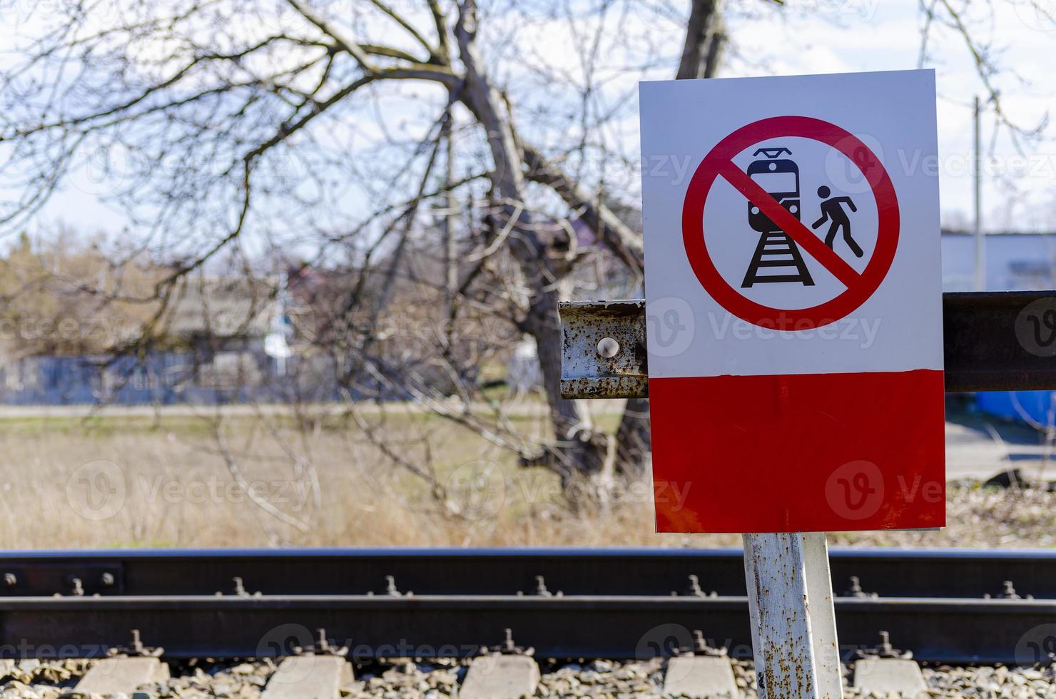 un rojo firmar con un negro silueta de un persona pisar en el ferrocarril pistas, cuales prohíbe pasajeros o otro personas desde cruce el ferrocarril pistas cuadrado firmar, antecedentes de árboles, la seguridad en foto