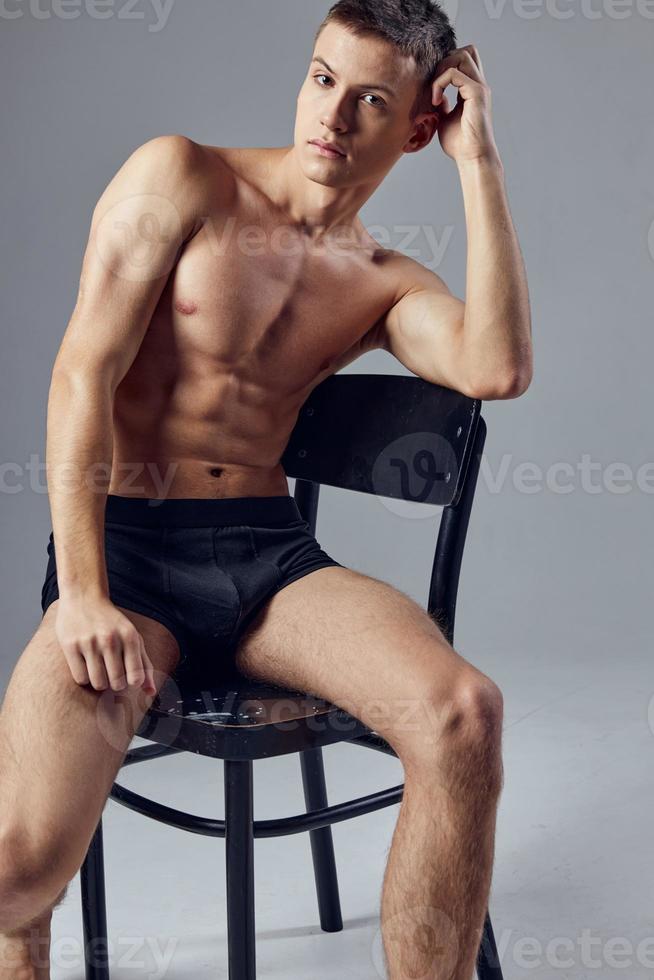 an attractive athletic man sits on a chair with his elbows on the back photo