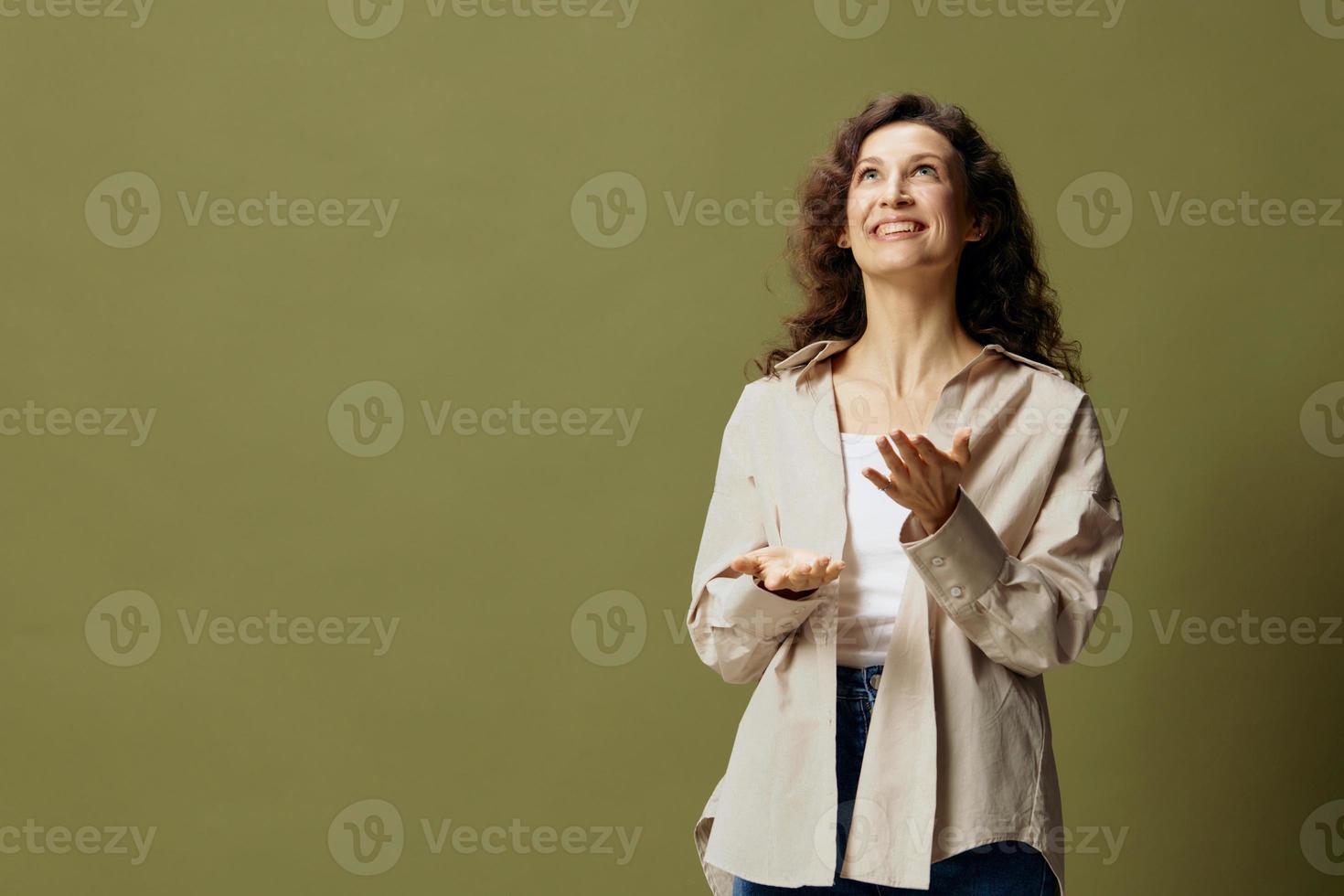 Overjoyed shocked happy curly beautiful female in linen casual shirt gestures while communicating looks aside posing isolated on olive green pastel background. People Lifestyle Emotions. Copy space photo