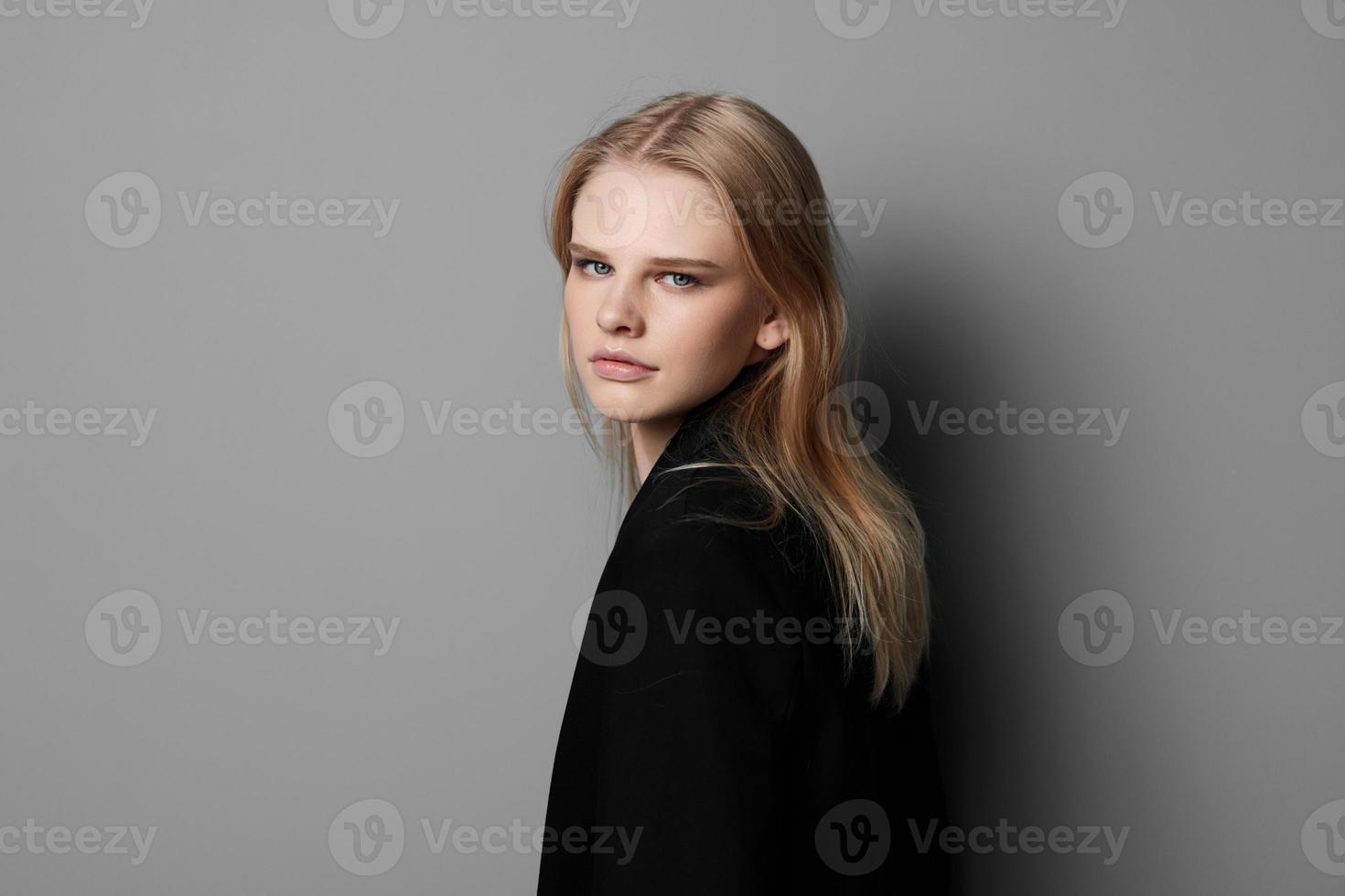 Young expressive beautiful blonde professional model posing isolated in studio dressing in black jacket looks at camera. Fashion Minimalistic concept photo