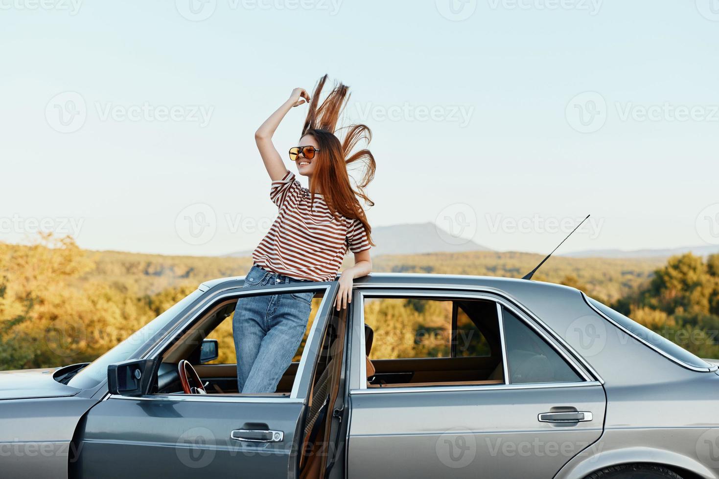 Happy woman traveler climbed on the car and spread her arms smiling happily. looks at the nature around. Lifestyle in travel and joy photo