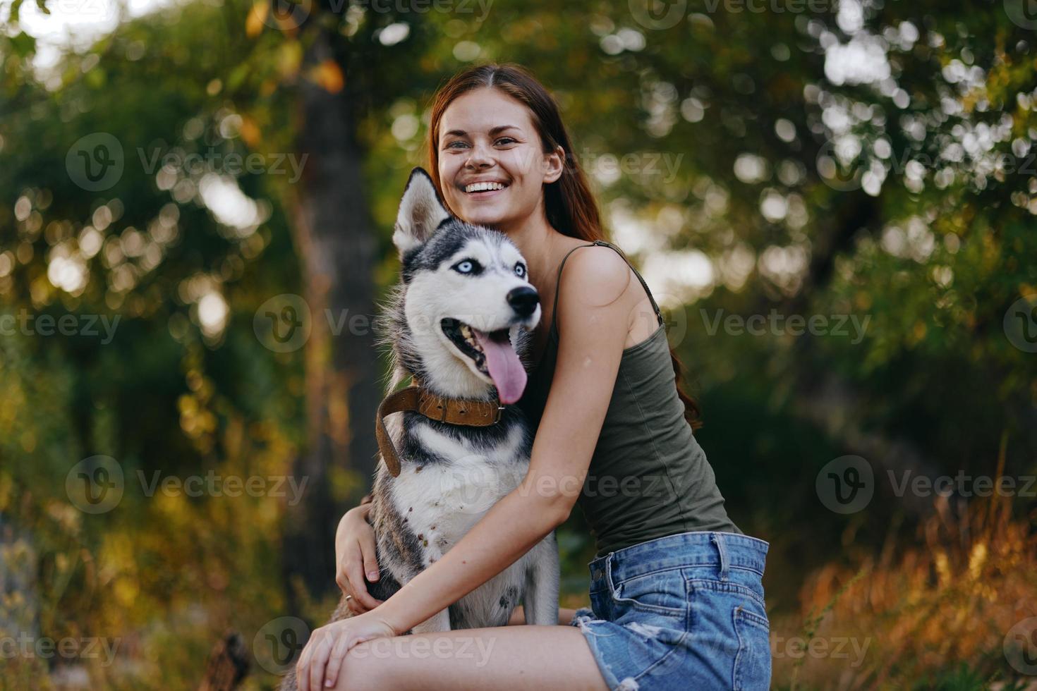 Joyful woman with a husky breed dog smiling while sitting in nature on a walk with a dog on a leash autumn landscape on the background photo