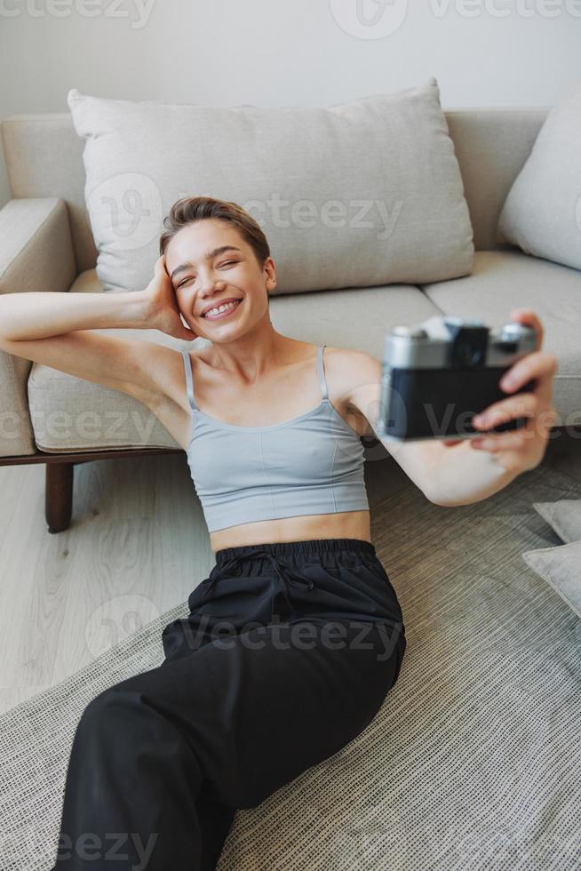Happy smile woman holding an old camera and taking pictures of herself as a weekend photographer in home clothes with a short haircut hair without filters on a white background, free copy space photo
