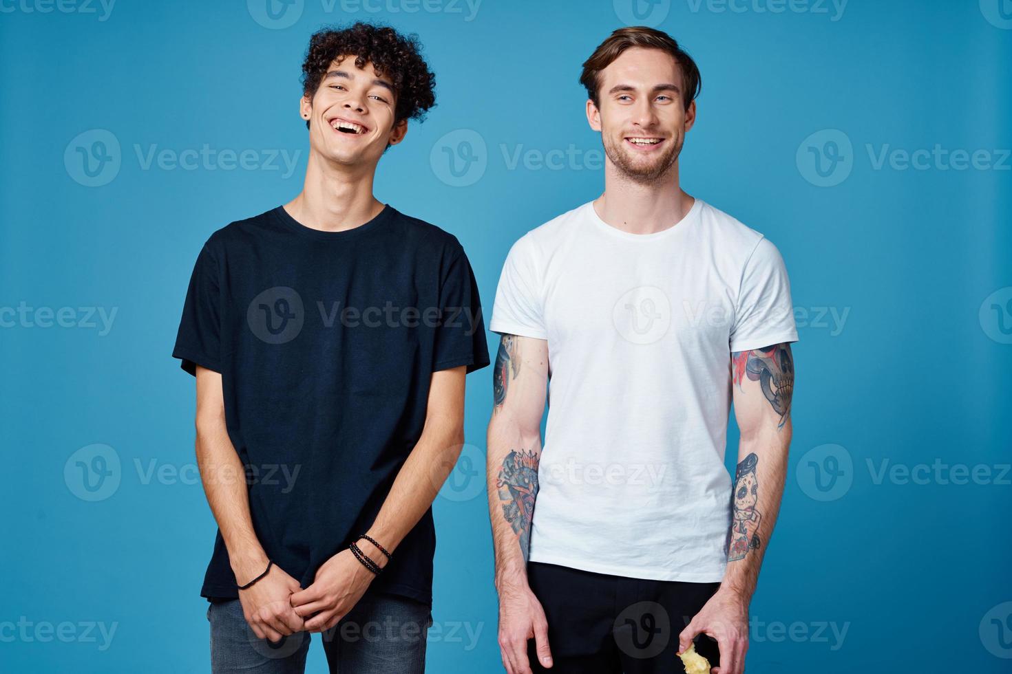curly guy in a black t-shirt and a man with a tattoo on a blue background friends chatting photo