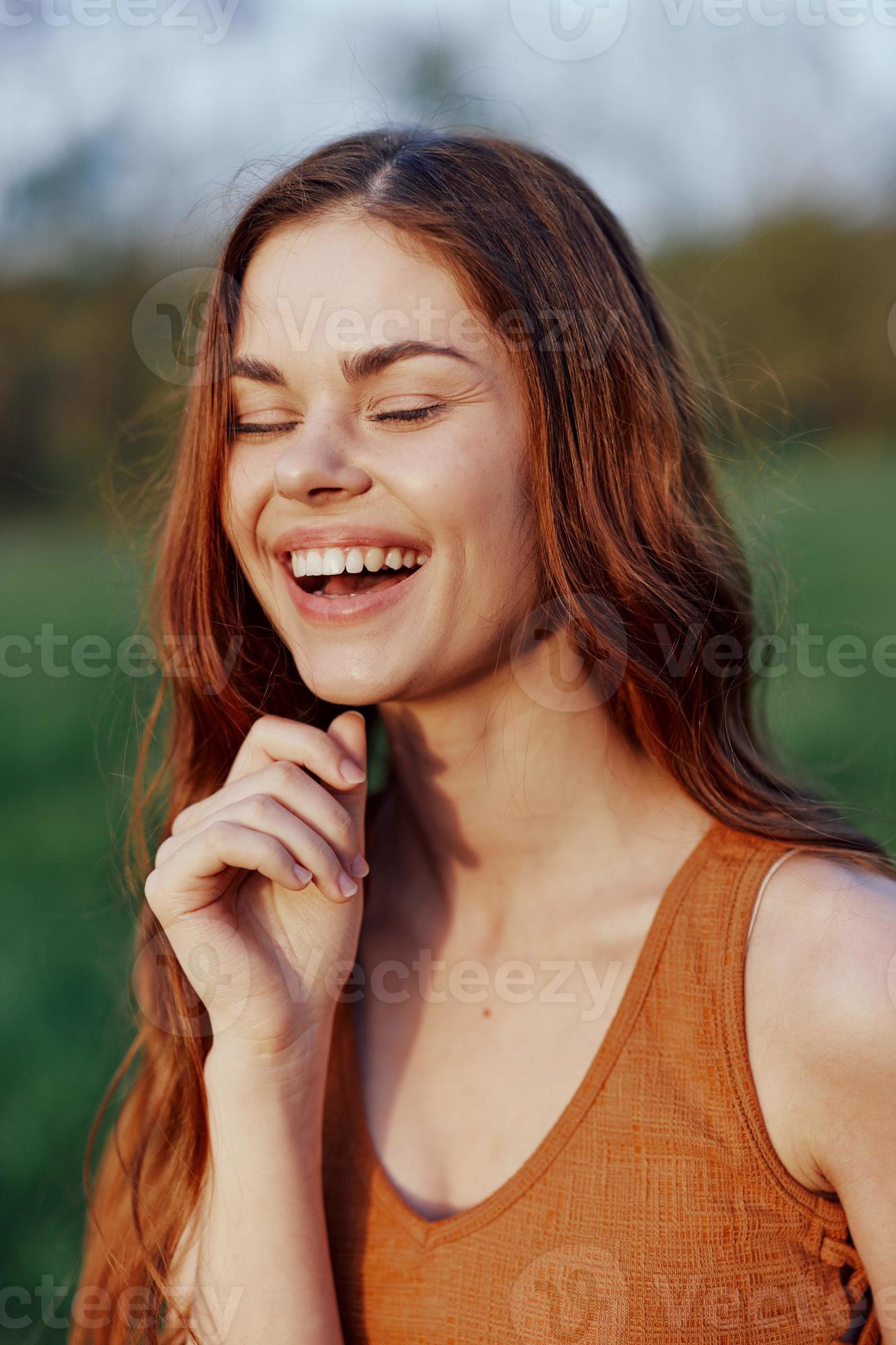 Closeup portrait of a smiling young woman with eyes closed in the sun with red hair in nature