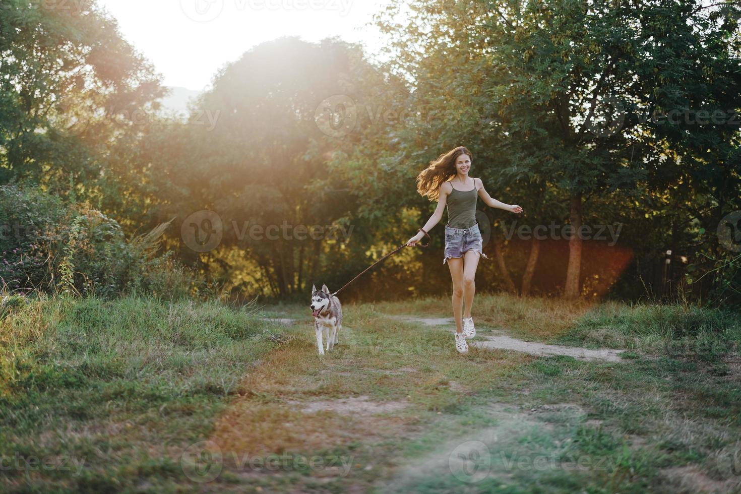 Woman and her husky dog happily running through the grass in nature in the park smile with teeth fall walk with pet, traveling with a dog friend photo