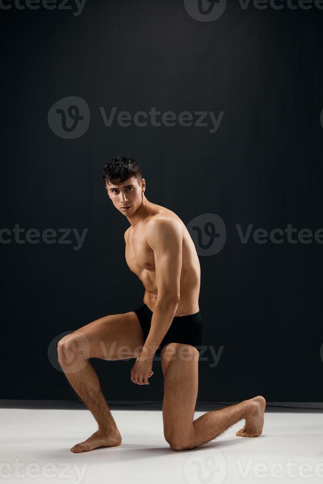 man in black shorts kneels on a dark background photo