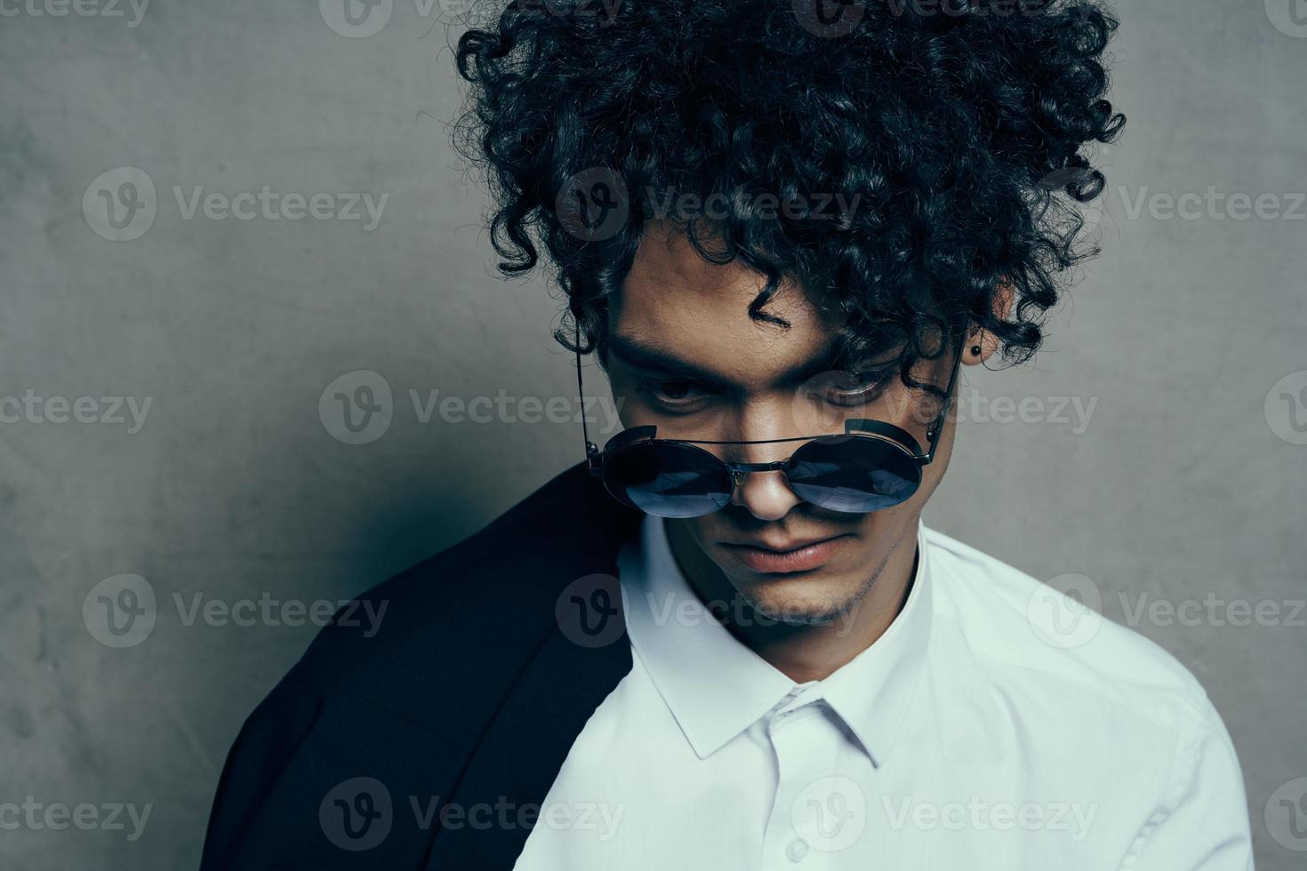 portrait of a curly-haired guy in a shirt with a jacket on his shoulder and glasses on his face close-up photo