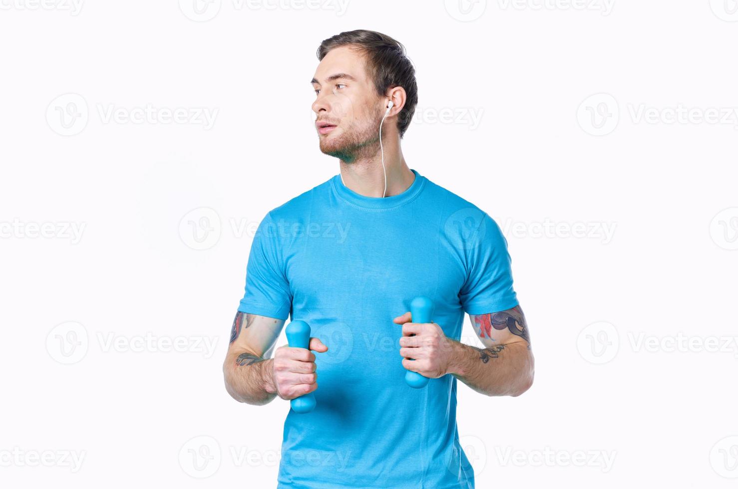 man with dumbbells in a blue t-shirt on a light background looking to the side cropped view photo