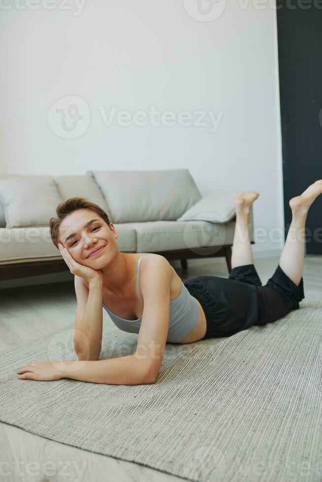 Teenage girl lying on the floor at home smiling in home clothes with a short haircut, lifestyle without filters, free copy space photo