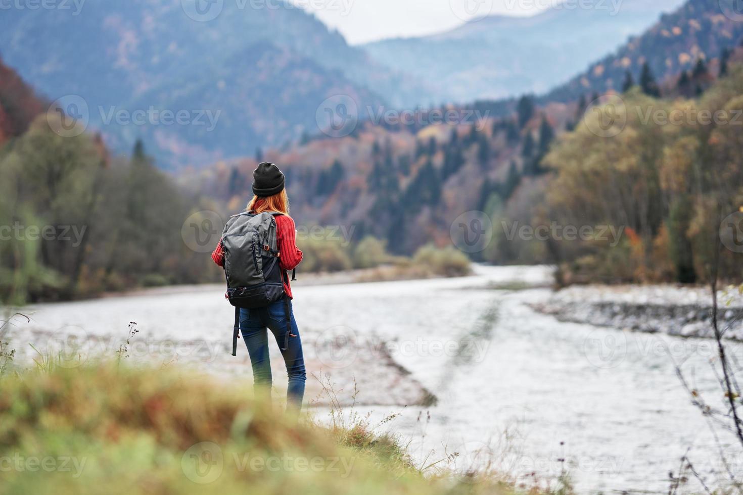 young traveler with a backpack in jeans and a sweater near the river in the mountains photo